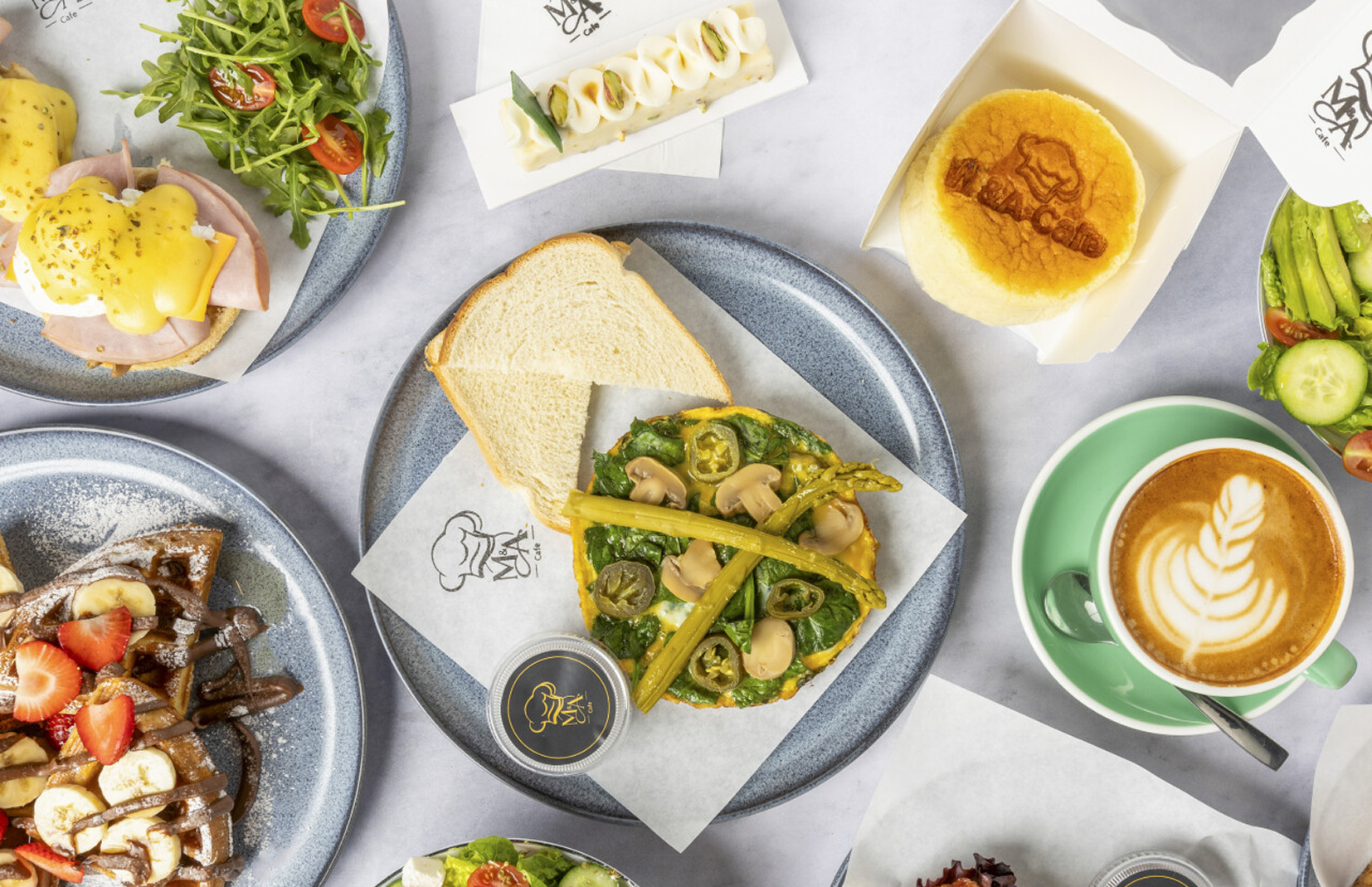 Overhead view of M&A Café's signature dishes including omelets, eggs benedict, latte art, and fresh salads
